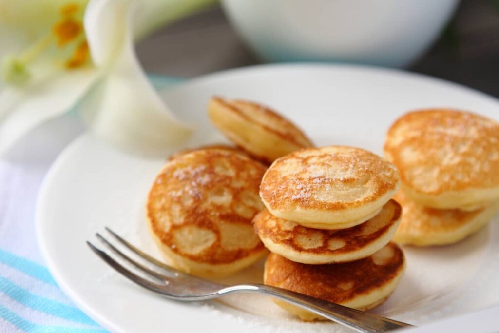 Plate of mini pancakes dusted with powdered sugar and a fork on the side