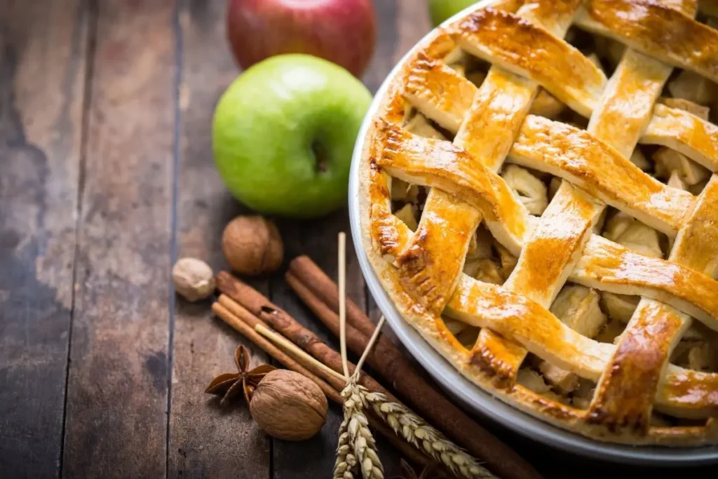 Freshly baked apple pie with lattice crust and green apples in the background.