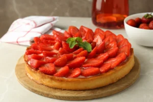  A fresh strawberry tart garnished with mint leaves on a wooden board.