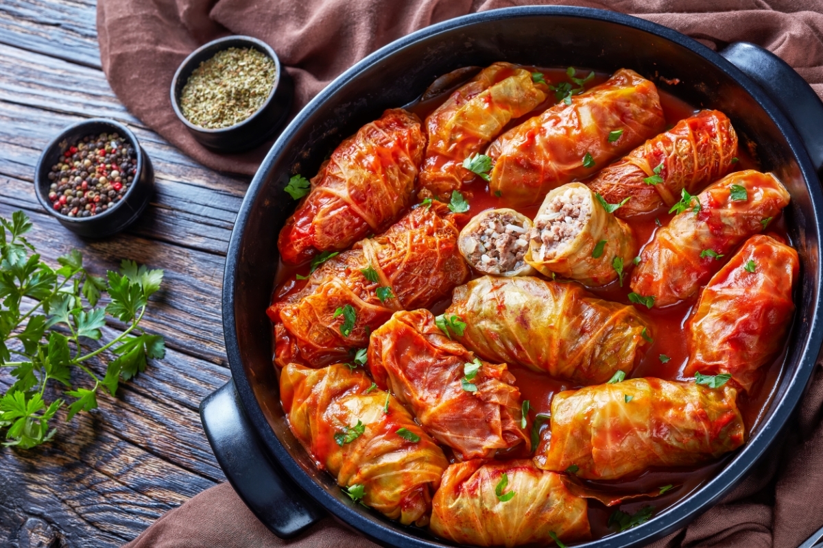 Stuffed cabbage rolls in tomato sauce garnished with parsley, served in a black pan on a rustic wooden table with spices and herbs on the side