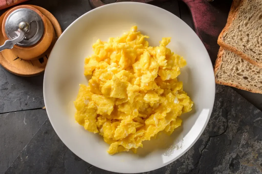 Plate of golden scrambled eggs served alongside slices of whole grain bread