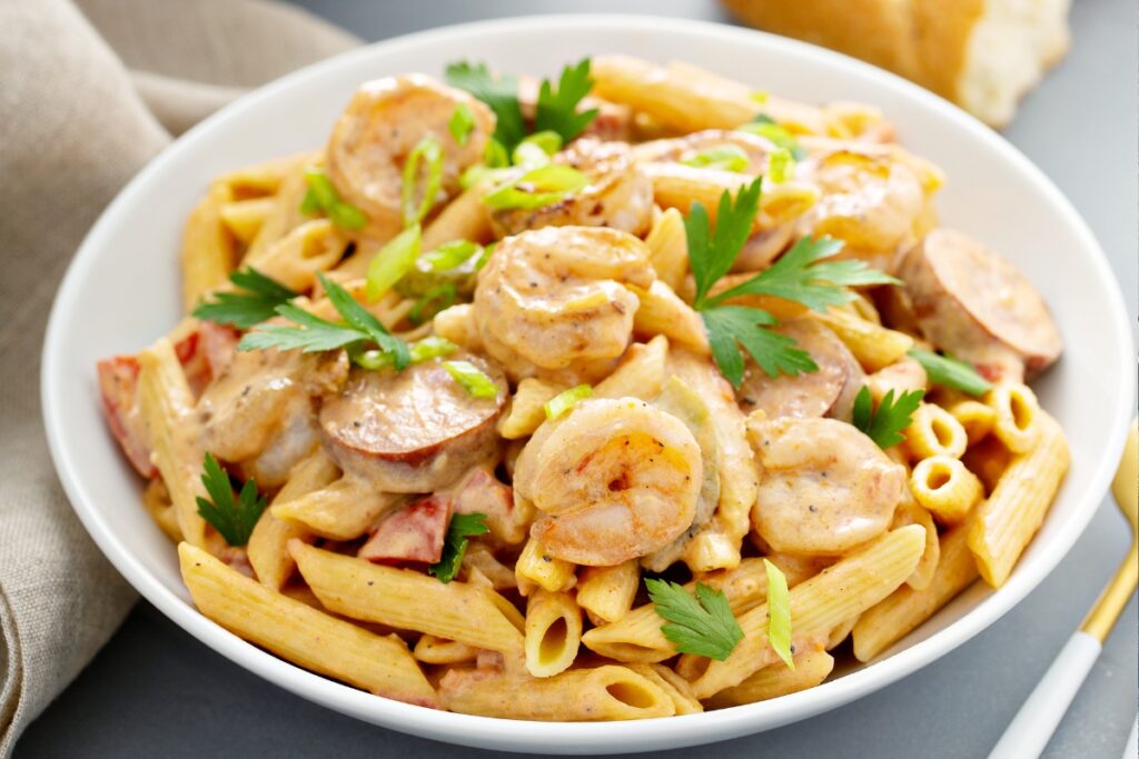 A close-up of Cajun Shrimp Pasta with creamy sauce, featuring shrimp, sausage slices, and garnished with fresh parsley and green onions.