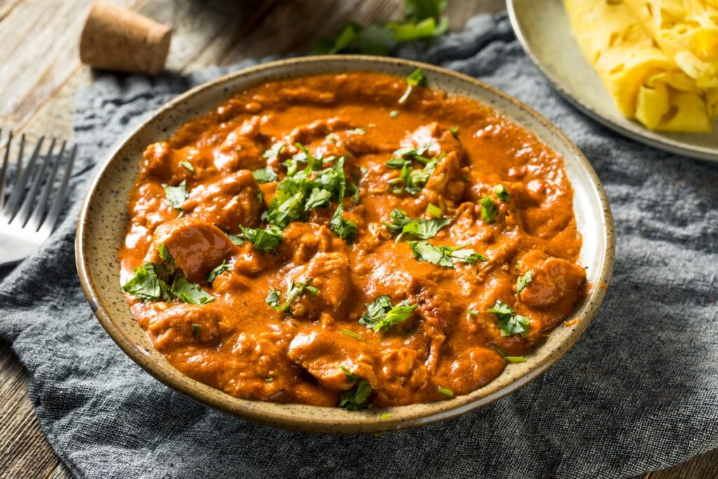 A bowl of vibrant butter chicken in a creamy tomato-based sauce, garnished with fresh cilantro, served on a rustic table setting.