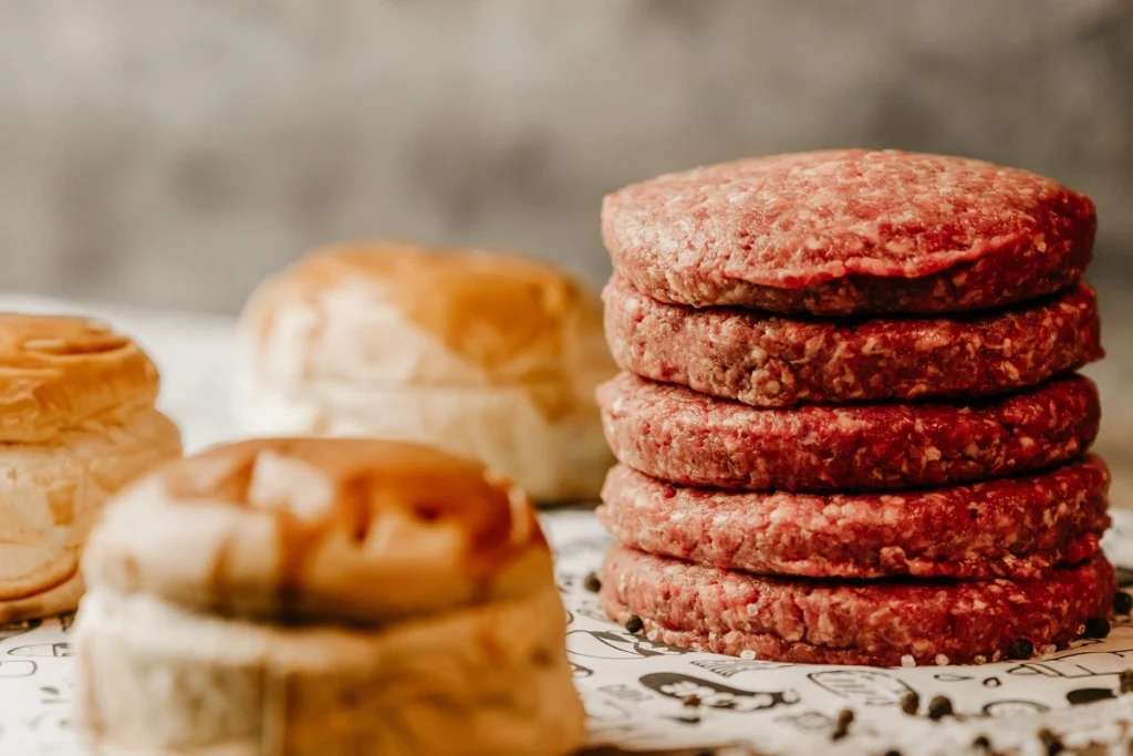 Raw turkey sausage patties stacked on parchment paper, with burger buns in the background.