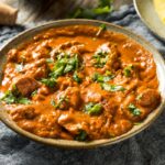 A bowl of vibrant butter chicken in a creamy tomato-based sauce, garnished with fresh cilantro, served on a rustic table setting.