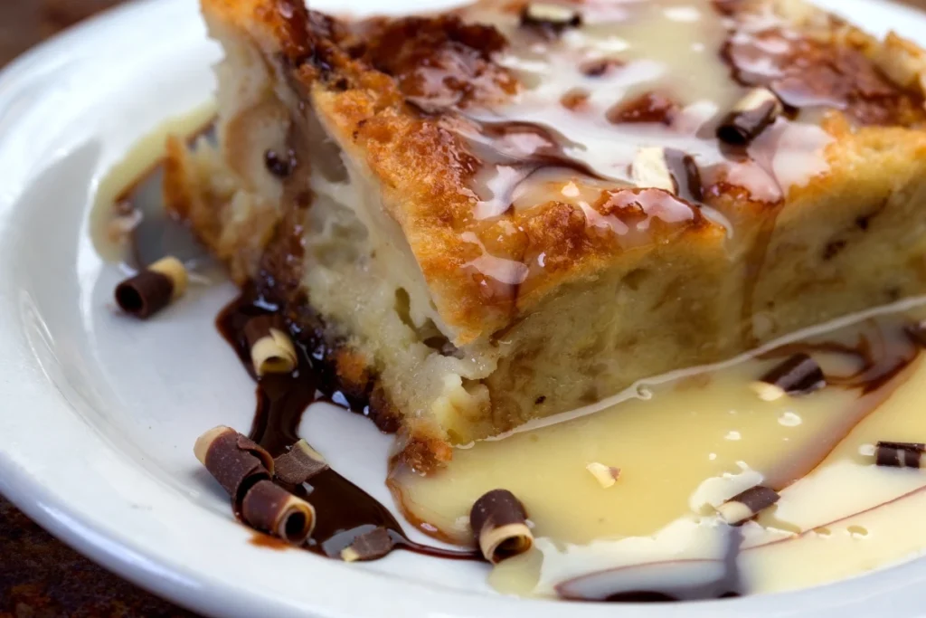  A slice of white chocolate bread pudding with white and dark chocolate drizzle and chocolate curls.