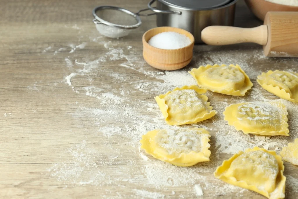 Uncooked lobster ravioli on a wooden surface with kitchen tools.