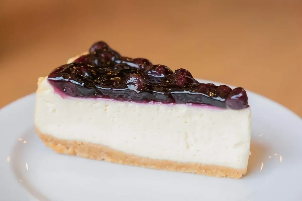 A slice of blueberry-topped cheesecake on a white plate.