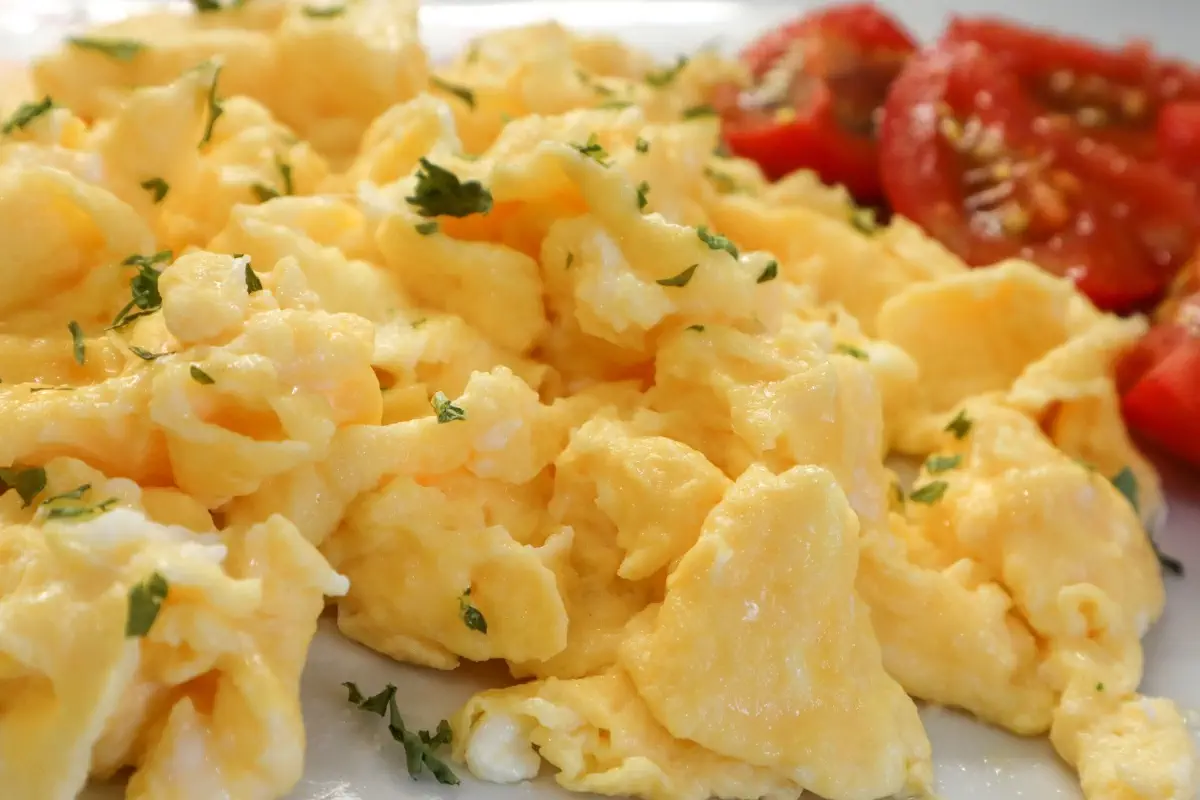 Fluffy scrambled eggs garnished with fresh herbs and served with sliced tomatoes