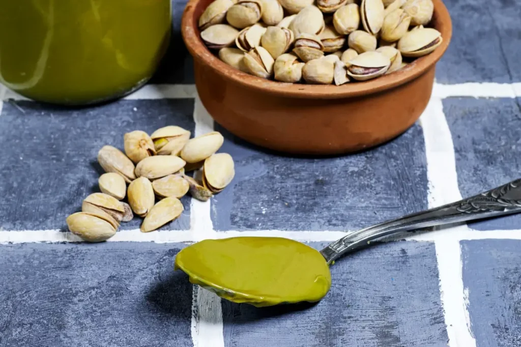 Spoon of creamy pistachio spread next to a bowl of whole pistachios