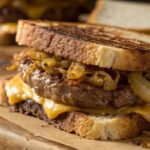 Close-up of a patty melt sandwich with grilled onions and melted cheese.