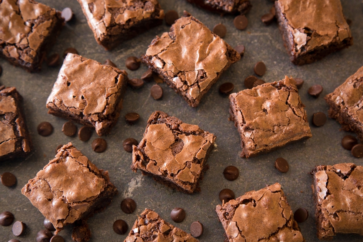 Fudgy chocolate brownies with a crackled top, scattered with chocolate chips on a dark surface.