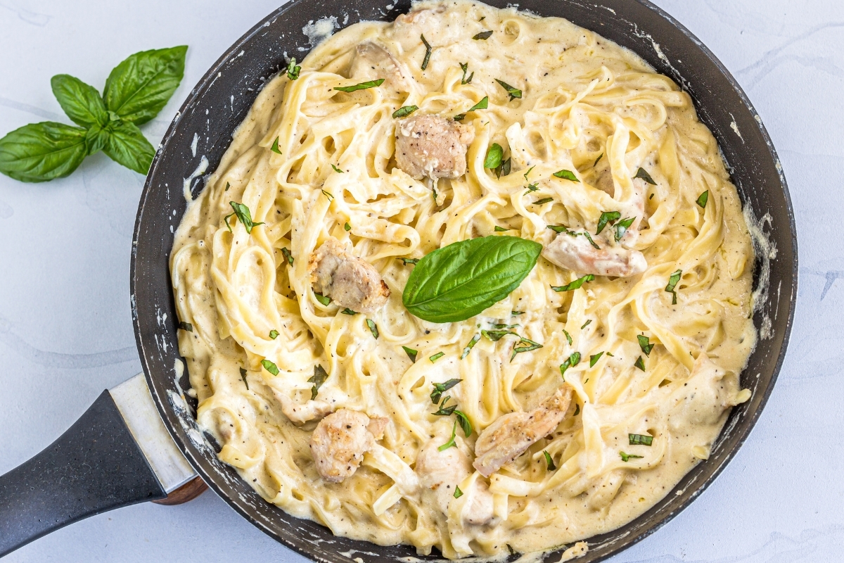 Creamy parmesan chicken pasta topped with fresh basil in a black skillet.