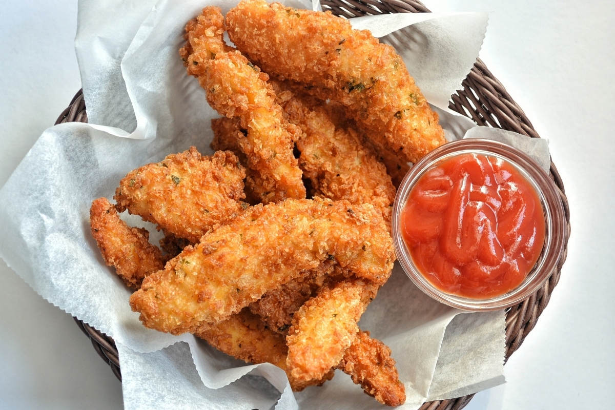 Crispy golden-brown chicken tenders served in a basket with a side of ketchup.