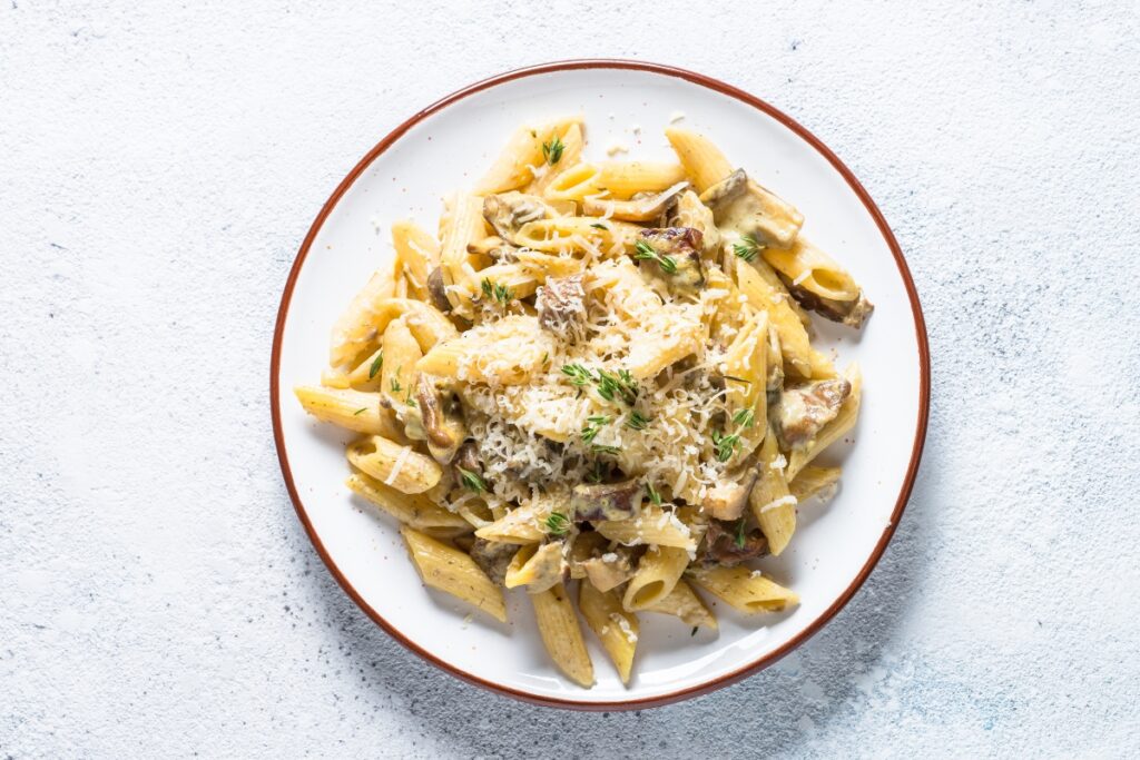 Penne pasta with creamy mushroom sauce, topped with grated cheese and fresh thyme on a white plate.