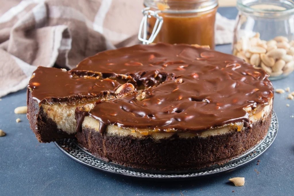 A whole Snickers Cheesecake with a slice removed, revealing its creamy interior.