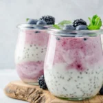 Glass jars filled with layered yogurt, berry puree, and chia seeds, topped with fresh blueberries and mint.