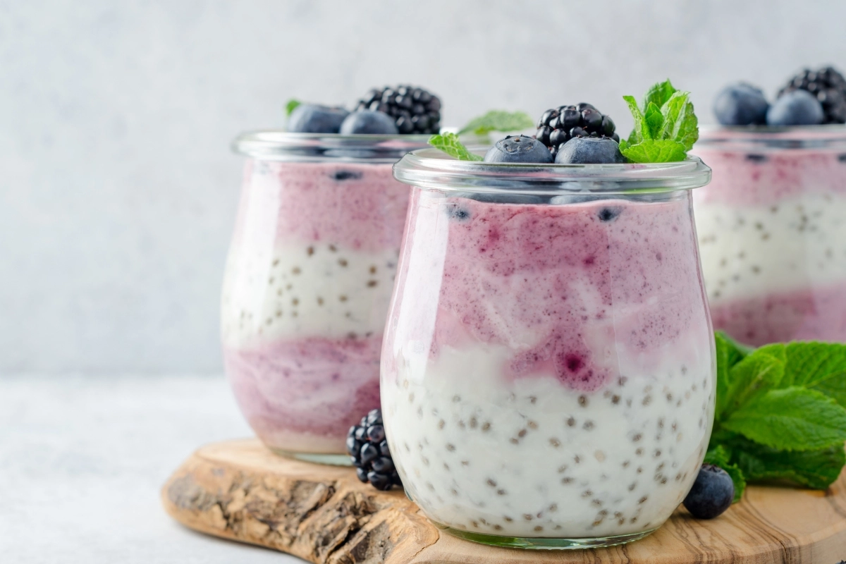 Glass jars filled with layered yogurt, berry puree, and chia seeds, topped with fresh blueberries and mint.