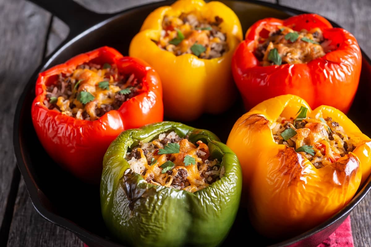 Stuffed bell peppers with cheese and rice filling in a cast-iron skillet.