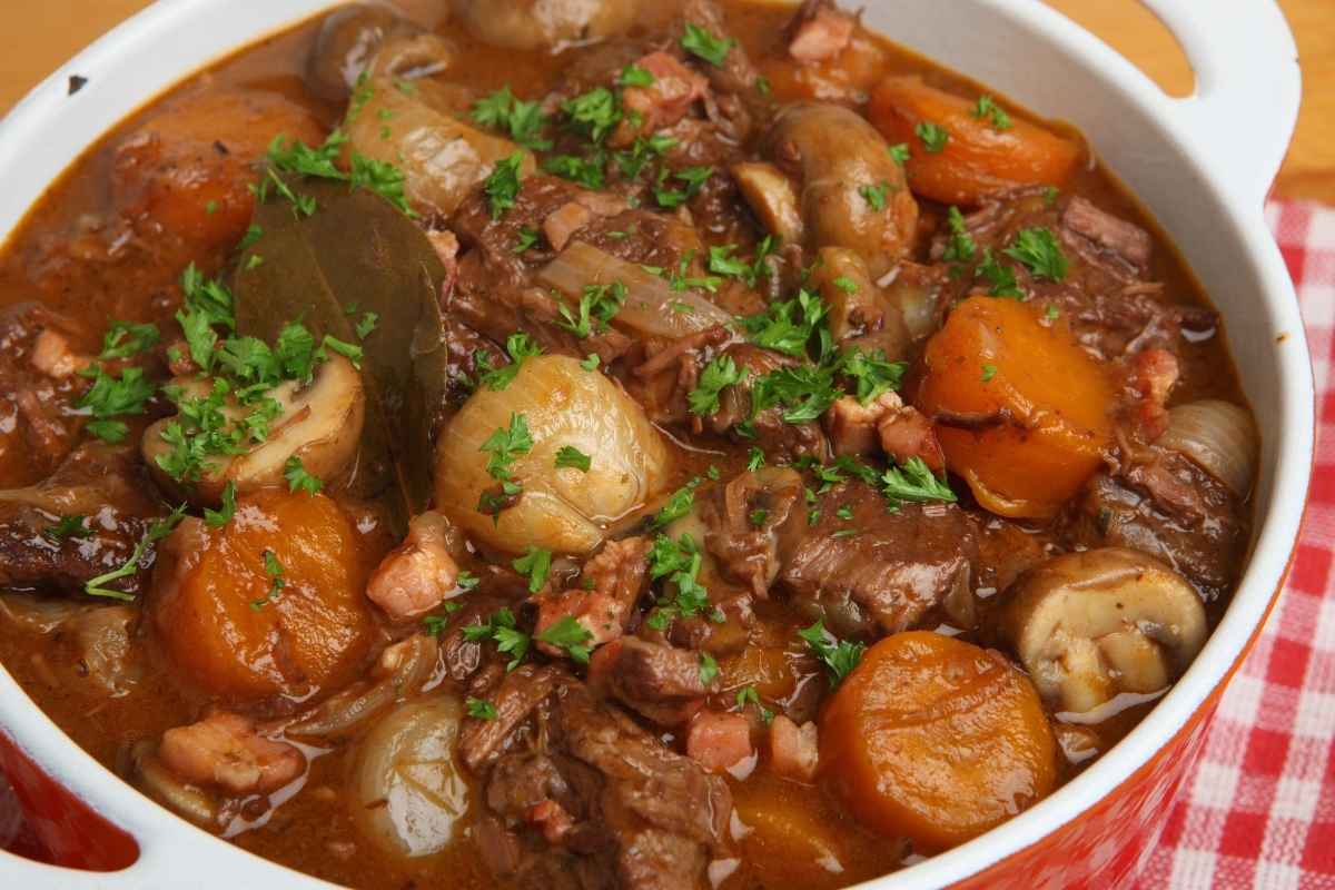 A rich and hearty beef stew with carrots, onions, mushrooms, and fresh herbs in a red Dutch oven.