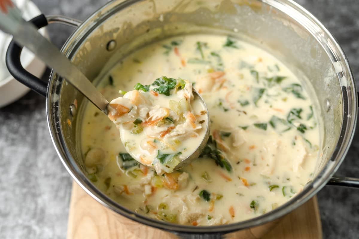 Creamy chicken gnocchi soup in a stainless steel pot with a ladle serving a portion.