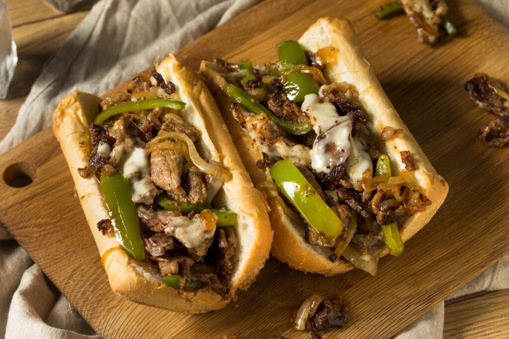 Philly cheesesteak sandwiches with sautéed onions, green bell peppers, and melted cheese on a toasted hoagie roll.