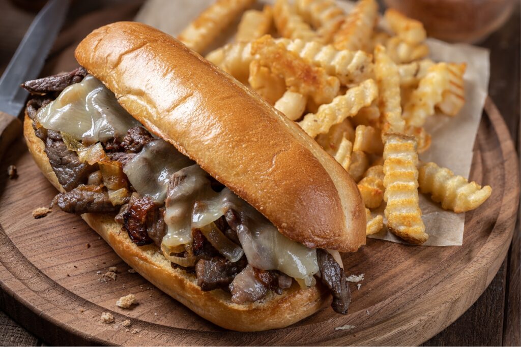 Philly cheesesteak sandwich with melted cheese and caramelized onions, served with crispy crinkle-cut fries.