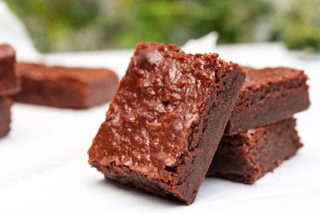 Classic fudgy brownies with a crackly top, stacked on a white surface.
